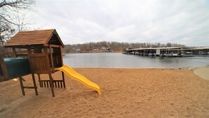 A sandy beach area with a wooden play structure and a yellow slide. - 2 bed King Master/2 bath condo with lake access and large 16 x 40 boat slip (Osage Beach)