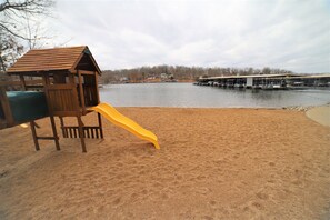Guests can enjoy a beachside play area with a slide and a dock with boats nearby.
