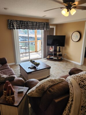 Relax in this stylish living room with a large flat-screen TV, comfortable sofa, and sliding glass door leading to a balcony with outdoor furniture.