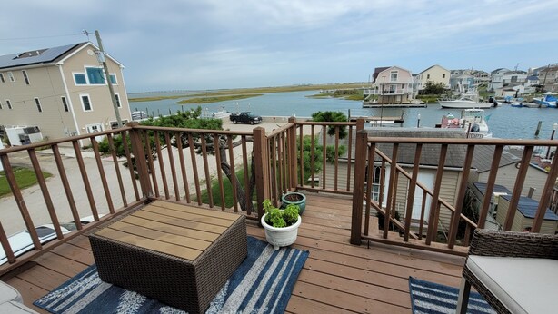 Une terrasse en bois avec des meubles d’extérieur, un pot de fleurs et une vue sur une marina où sont amarrés des bateaux.