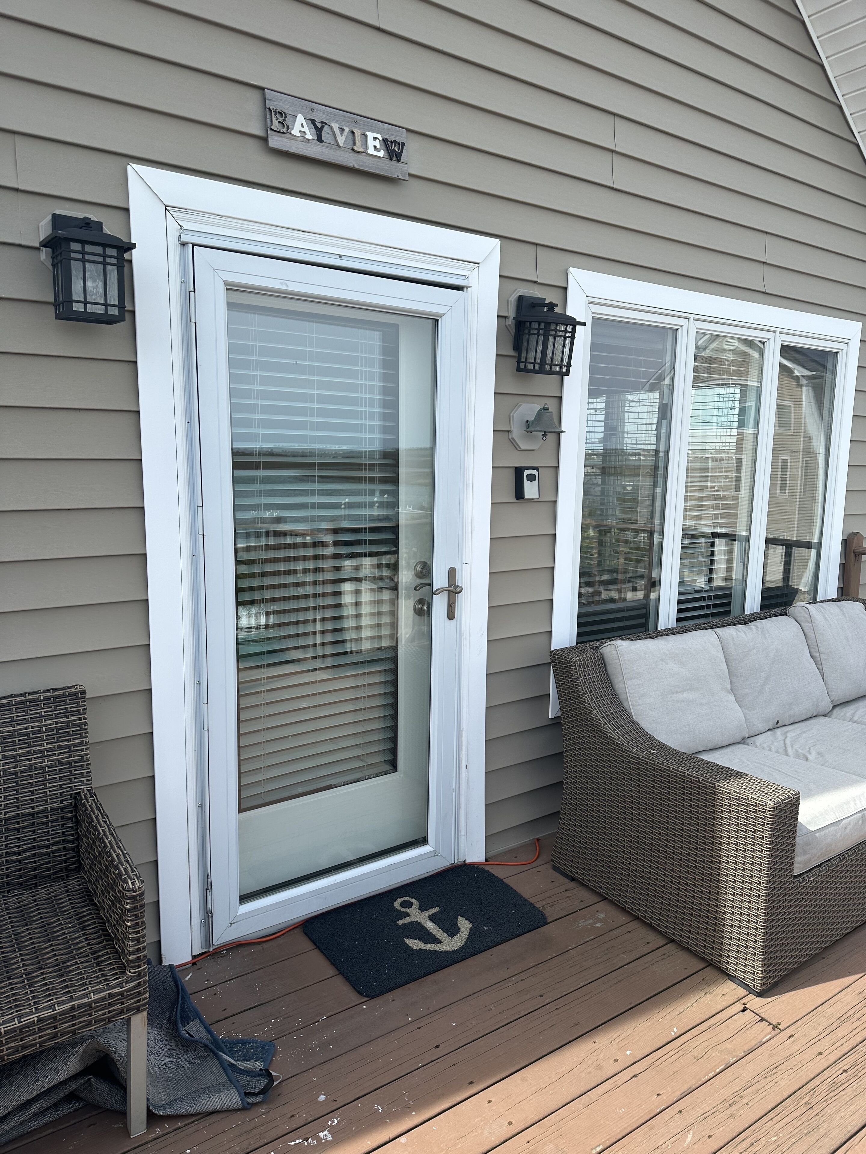 A house with a 'BAYVIEW' sign, a sliding glass door, a wicker sofa, and a doormat with an anchor symbol.