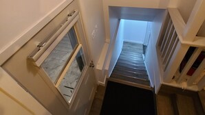 Een smalle trap met een raam aan de linkerkant en een deur onderaan.