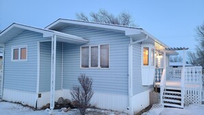 Een lichtblauwe bungalow met een veranda, een kleine tuin en een sneeuwbedekte voortuin.