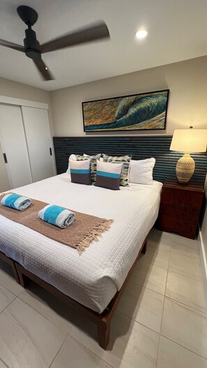 A hotel room with a bed, a ceiling fan, a painting, a nightstand, and a lamp.