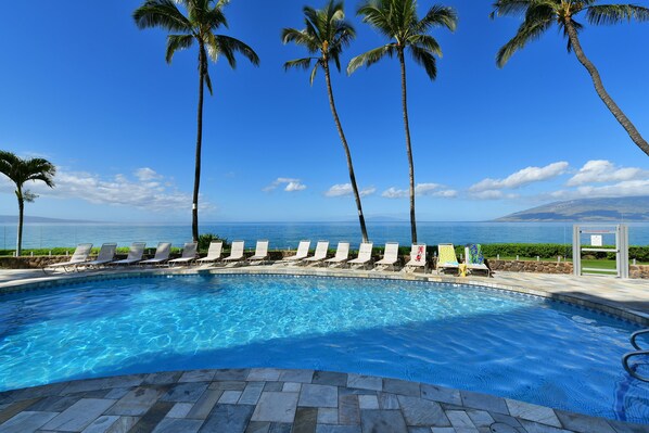 Relax by the ocean with unobstructed views from this serene pool area surrounded by lounge chairs and palm trees.