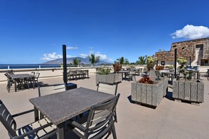 An outdoor patio with tables and chairs, overlooking a beach and a mountain.