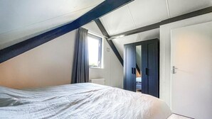 Ein Schlafzimmer mit schrägem Dach, einem Bett, einem Fenster mit Vorhängen und einer Tür.