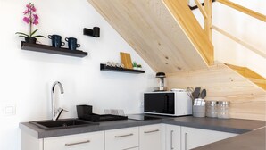 Cozinha moderna com pia embutida, micro-ondas e máquina de café. Há prateleiras com objetos decorativos e um vaso de planta.
