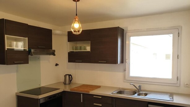 A compact kitchen with dark cabinetry, a built-in oven, a stovetop, a sink, and a window providing natural light. - Comfortable room near Paris and transport (Achères)