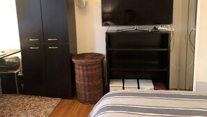 A bedroom with a bed, a TV, a wardrobe, and a wicker basket. - True 1Bdrm (New York)