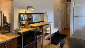 A compact kitchen with a microwave, stove, and a wooden countertop. There is a clock on the wall and a refrigerator in the background. - True 1Bdrm (New York)