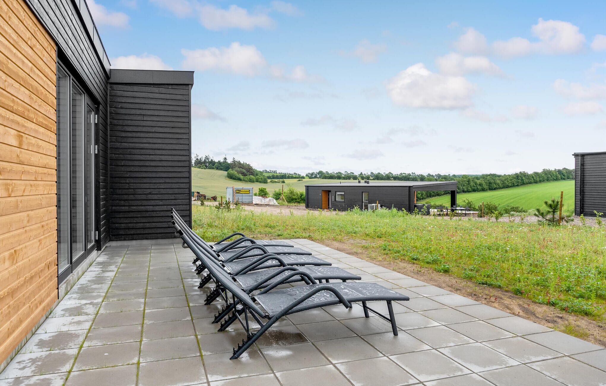 A covered outdoor seating area with metal chairs and tables, adjacent to a building with a wooden facade and a black exterior.