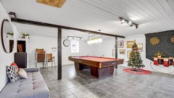 Et rummeligt værelse med billardbord, sofa, juletræ og dartskiver.