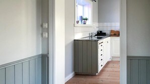 A narrow hallway with a wooden floor leading to a kitchen area with white cabinets and a window above the sink. - Gorgeous home in Rättvik with lake view (Rättvik)