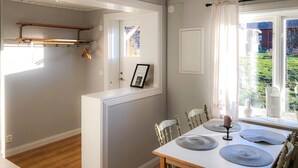 A dining area with a white table, four chairs, and a view of a garden through a window with white curtains. - Gorgeous home in Rättvik with lake view (Rättvik)