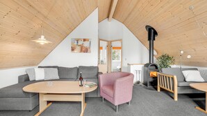 A cozy loft-style room with a high ceiling, a black wood-burning stove, grey sofas, a round wooden coffee table, and a pink armchair. - 4 bedroom awesome home in Gråsten (Gråsten)