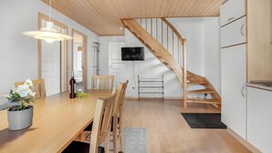 A modern kitchen with wooden flooring, a dining area with a wooden table and chairs, a staircase, and a TV mounted on the wall. - 4 bedroom awesome home in Gråsten (Gråsten)
