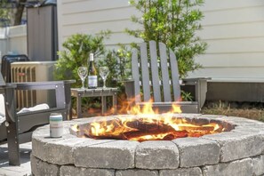 A stone fire pit with a can of beer and two glasses of wine on a table nearby.