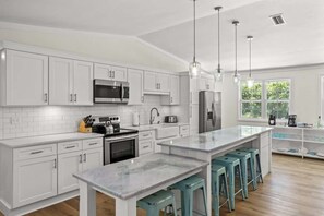 Una cocina moderna con armarios blancos, electrodomésticos de acero inoxidable, una isla de mármol y taburetes de bar color turquesa.