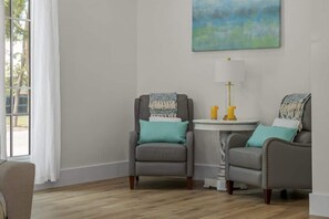 A room with two armchairs, a small round table, a lamp, and a painting on the wall.