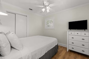 A bedroom with a bed, a TV on a dresser, a ceiling fan, and a window with blinds.