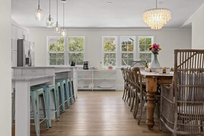 A kitchen with a central island, bar stools, a dining table with chairs, and a chandelier.