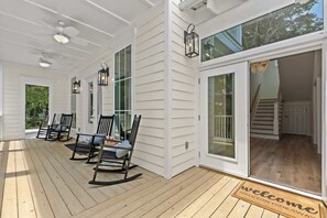 A covered porch with rocking chairs, a wooden deck, and a sliding glass door leading to a staircase.