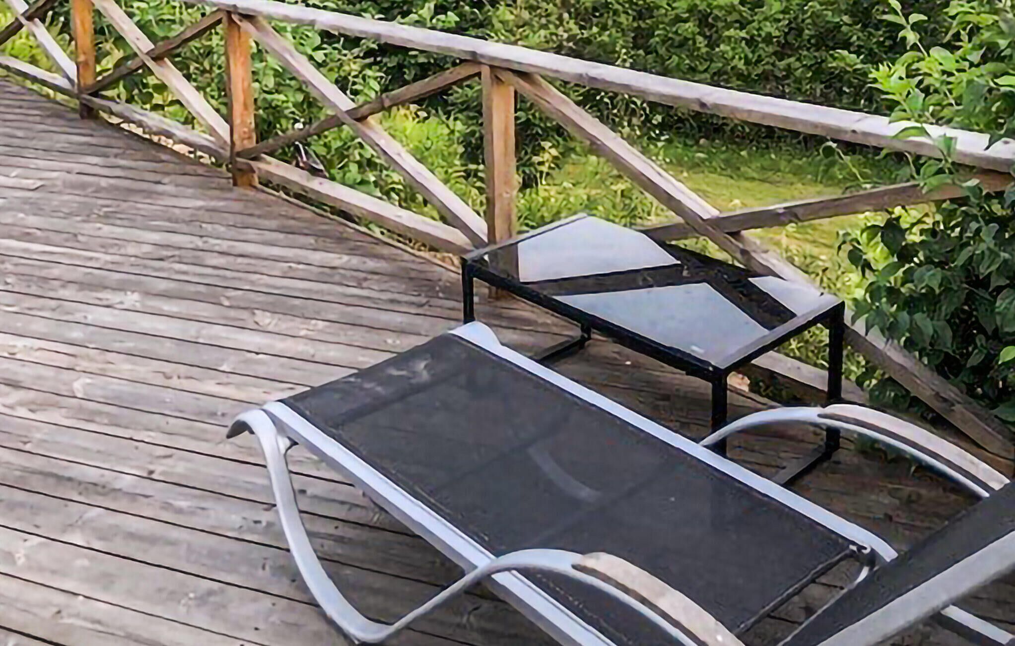 A wooden deck with two black lounge chairs and a small table.