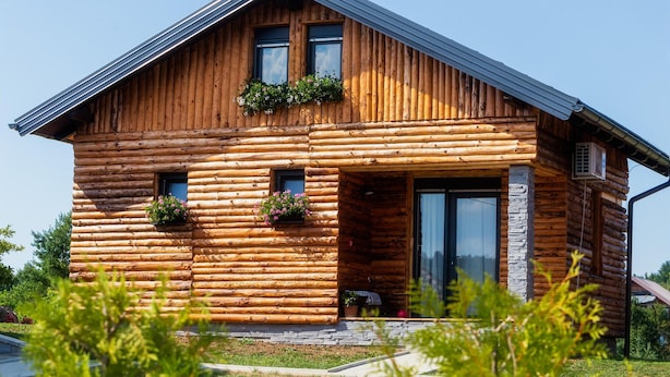 Eine Blockhütte mit geneigtem Dach, großen Fenstern und Blumenkästen an der Vorderseite.