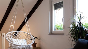 Ein Zimmer mit Hängekorbsessel, Jalousien an einem Fenster und einem Blumentopf.
