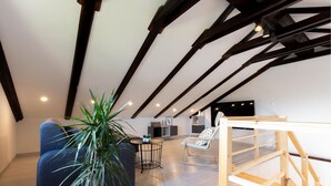 Ein Loft-Wohnraum mit freiliegenden Holzbalken, einer großen Topfpflanze, einer Couch, einem kleinen runden Tisch und einer Holzkonstruktion.