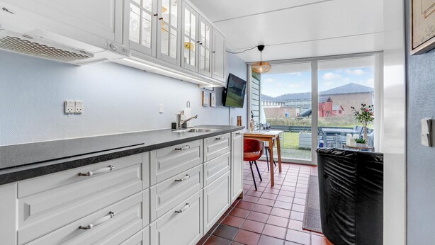 A modern kitchen with white cabinetry, a black countertop, and a large window overlooking a garden. - 1 bedroom beautiful home in Fanø (Fanø)