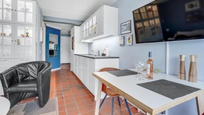 A modern kitchen with white cabinets, a dining area with a table and chairs, and a TV mounted on the wall. - 1 bedroom beautiful home in Fanø (Fanø)