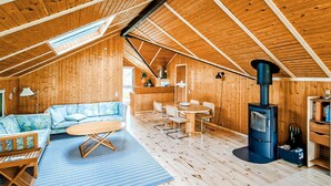 A wooden cabin interior with a sofa, dining table, chairs, a fireplace, and a skylight. - 3 bedroom gorgeous home in Væggerløse (Væggerløse)