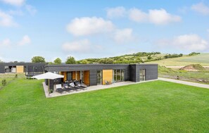 Ein modernes Haus mit einer Terrasse, Sitzgelegenheit und einem Trampolin.