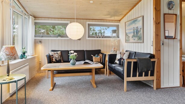A cozy living room with a wooden ceiling, a black leather sofa, a wooden coffee table, and a large window with curtains.