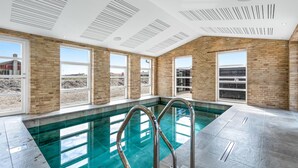 Une piscine intérieure moderne avec des parois en verre transparent, un mur en briques et un plafond doté d’un système de ventilation.