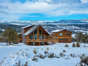 A large wooden cabin with a balcony and a garage, surrounded by snow-covered landscape and mountains. - Copper Rock Ridge |Hot Tub |Pool Table| Near Zion (Orderville)