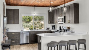 A modern kitchen with dark cabinets, a white countertop, and a large island with bar stools. - Painted Cliffs| Zion & Bryce |Fire Pit |Hot Tub| (Orderville)