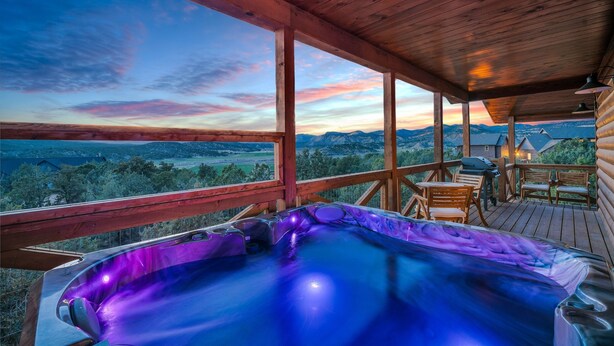 En træterrasse med jacuzzi, udendørs møbler og en smuk udsigt til bjerge.