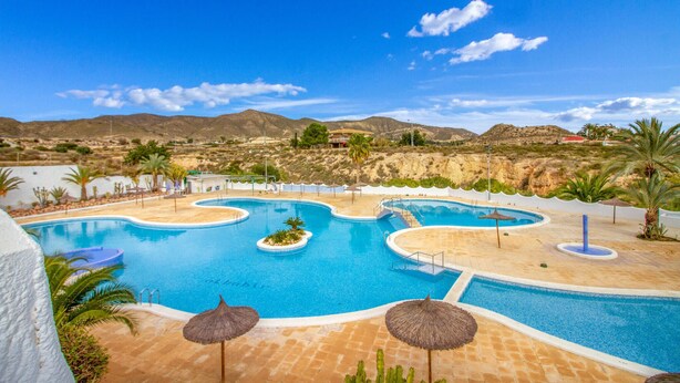 Et resortområde med flere swimmingpools, palmer og et bjergrigt landskab i baggrunden.