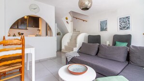 En moderne stue med sofa, spisebord med stole, trappe og et køkkenområde.