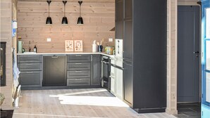 Eine moderne Küche mit dunklen Schränken, einem eingebauten Backofen und einem Kühlschrank. Drei Pendelleuchten sind an der Decke angebracht.