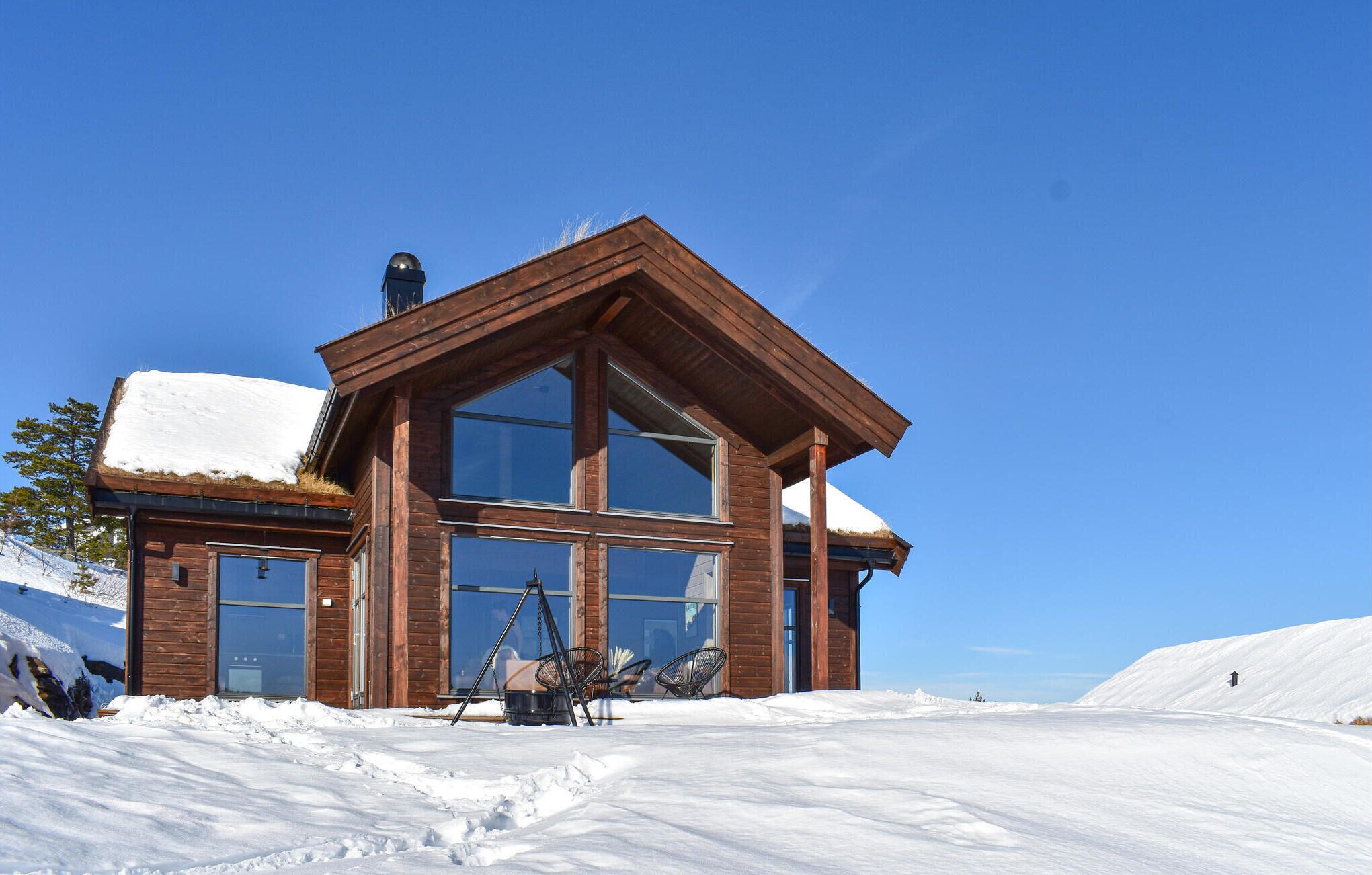 Een houten hut met grote ramen en een sneeuwbedekte dak, omgeven door sneeuw.