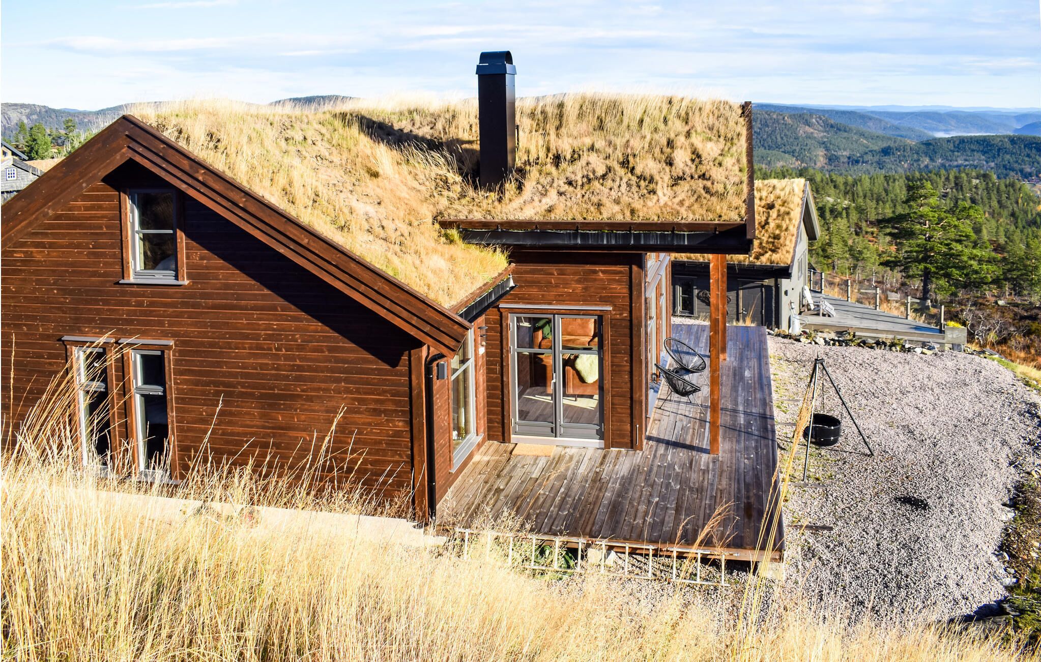 A wooden cabin with a grass roof, a wooden deck, and a view of the surrounding hills.