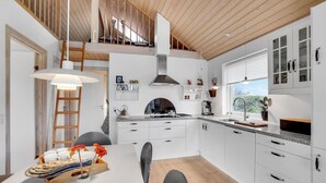 A modern kitchen with white cabinetry, a wooden ceiling, and a dining area with a table set for four. - 2 bedroom beautiful home in Kerteminde (Kerteminde)