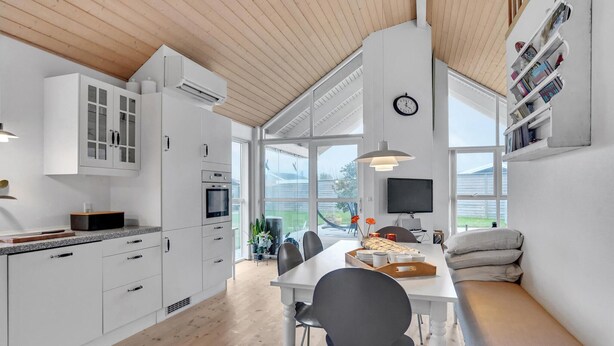 A modern kitchen with white cabinets, a built-in oven, and a dining area with a table and chairs. - 2 bedroom beautiful home in Kerteminde (Kerteminde)