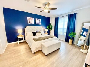 Relax in this serene bedroom with a large bed, tufted headboard, and a potted plant.