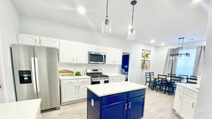 Une cuisine moderne avec des meubles blancs, un îlot central bleu, des appareils en acier inoxydable et des luminaires suspendus.