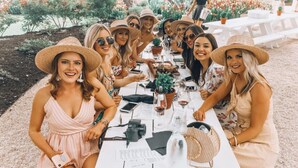 Un groupe de personnes est assis autour d’une table blanche à l’extérieur, avec un jardin en arrière-plan.